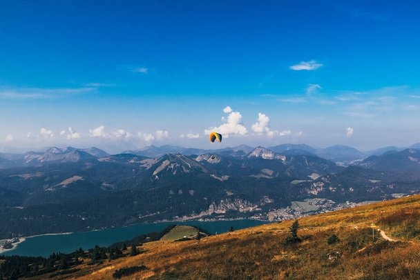 paracaidista con su colorido paracaídas vuela sobre el lago Wolfgangsee en la Alta Austria, cerca de la ciudad de Salzburgo. Posición inicial en la montaña Schafberg. Jugando con la vida. Deporte extremo. Día soleado. - Foto, Imagen