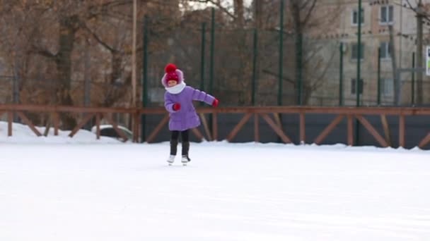 Ένα παιδί μαθαίνει να κάνει πατινάζ σε παγοδρόμιο. Κορίτσι πατίνια, πηγαίνει για χειμερινά σπορ - Πλάνα, βίντεο