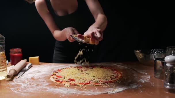 Sexy dona de casa com seios exuberantes em uma camiseta preta prepara uma deliciosa pizza e esfrega queijo duro em um ralador de ferro reto. Existem todos os ingredientes necessários e ferramentas de cozinha na mesa. - Filmagem, Vídeo