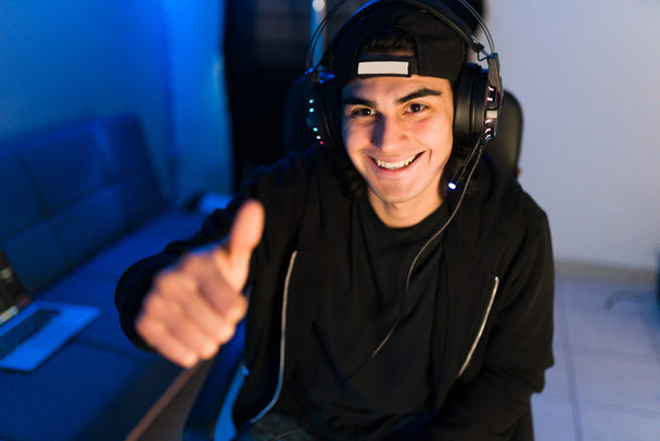 Portrait of an attractive latin gamer giving a thumbs up to the online viewers and friends on a webcam during a live stream of his online video game  - Photo, Image