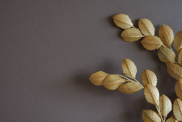 The branch with leaves is made of straw. Straw wall decoration. The products are made of straw. Decoration of straw on a gray background - Photo, Image