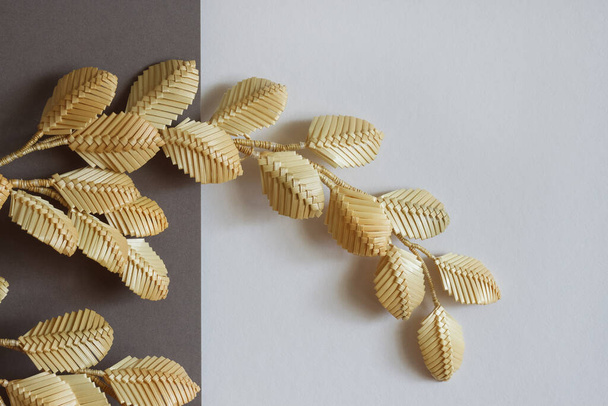 The branch with leaves is made of straw. Straw wall decoration. The products are made of straw. Decoration of straw on a gray white background - Photo, Image