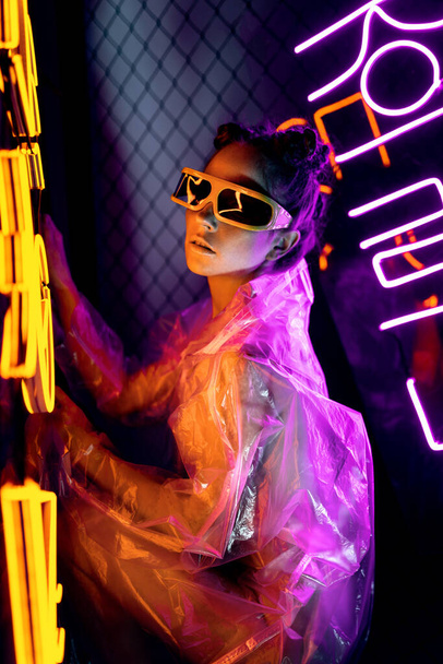 Retrato de uma jovem, vestida com roupas e óculos futuristas. Luz amarela e rosa néon. óculos de realidade virtual - Foto, Imagem