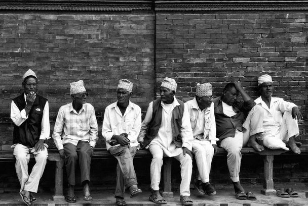 Einfarbige Reihe von Männern in traditioneller Kleidung auf einer Bank, Patan, Nepal. Hochwertiges Foto - Foto, Bild