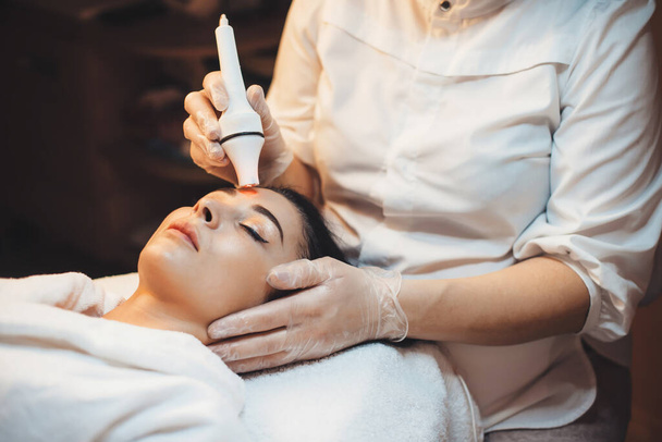 Procedimientos de tratamiento del acné realizados a una mujer acostada en un sofá en el centro de spa durante las sesiones de belleza - Foto, imagen