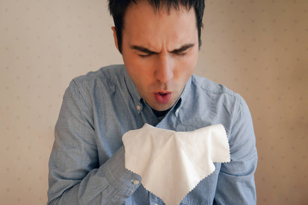 Il tousse. Jeune homme caucasien attrayant tousse intensément et couvre sa bouche avec une serviette. Rhume, grippe, mal de gorge, maladie respiratoire aiguë concept. éternuer dans un chiffon - Photo, image