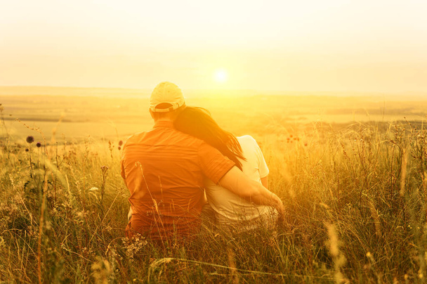 Birbirine aşık bir çift, tepede parlak turuncu günbatımının arka planında sarılıp oturuyor. Romantik yaz zamanı. Tanınmayan insanlar - Fotoğraf, Görsel