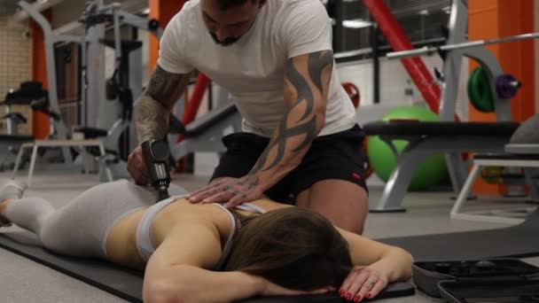 Personal trainer met behulp van massage pistool op het lichaam van sportvrouw - Video