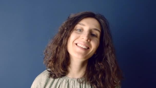 Retrato mulher close-up. Retrato de uma mulher europeia sorridente com cabelos longos encaracolados contra um fundo escuro. Mulher branca com cabelo escuro  - Filmagem, Vídeo