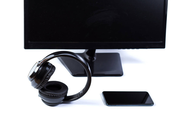 Czarne słuchawki bezprzewodowe ze smartfonem w pobliżu monitora PS na białym tle. - Zdjęcie, obraz