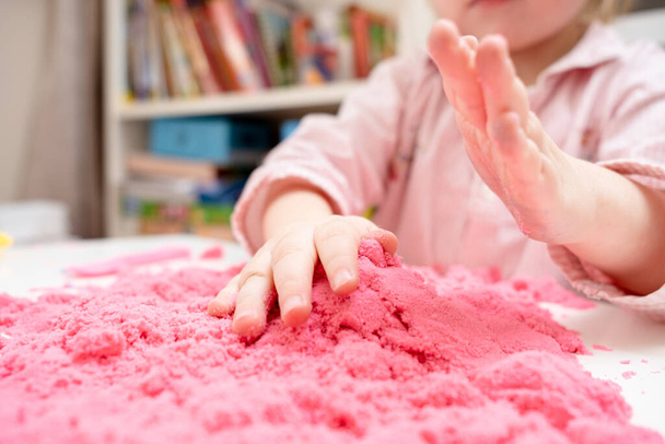 Entuzjastyczne dziecko bawi się różowym piaskiem kinetycznym. Koncepcja rozwijania umiejętności motorycznych i kreatywnej wyobraźni u dzieci. - Zdjęcie, obraz