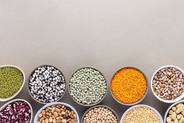 Different types of legumes in bowls, green and yellow peas, chickpeas and peanuts, colored beans and lentils, mung beans and beans, top view - Photo, Image