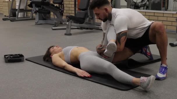 Personal trainer stretching legs of sportswoman in gym - Footage, Video