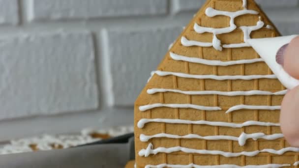 Kadın zencefilli kurabiye evini pasta çantasıyla, beyaz şeker şekeriyle, elleri beyaz tuğladan arkaplanla süslüyor. Noel tatili için ev yapımı zencefilli kurabiye pişirme. Yeni yıl gelenekleri - Video, Çekim