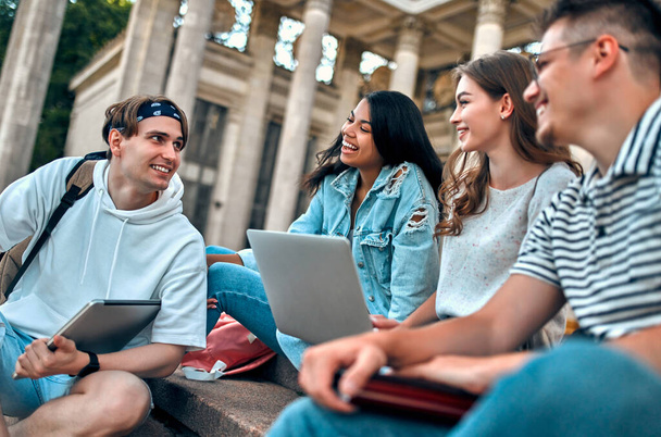 Um grupo de estudantes com laptops sentar-se nos degraus perto do campus e se comunicar. - Foto, Imagem