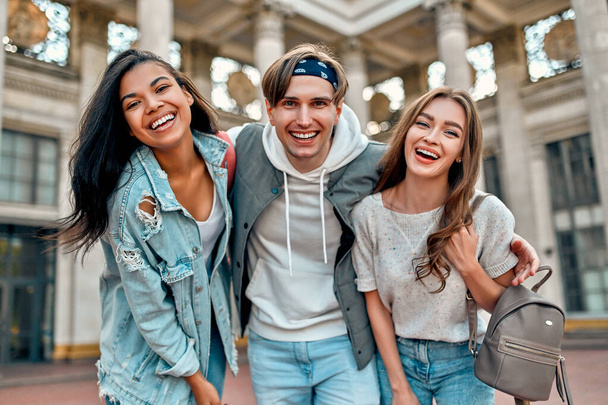 Un grupo de estudiantes en la calle cerca del campus universitario. Tres amigos están felices de conocer, abrazar y reír. - Foto, imagen