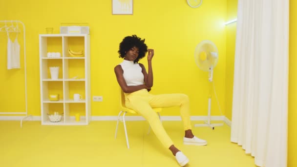 Afrikanerin sitzt in gelbem Büro und blickt in Kamera - Filmmaterial, Video