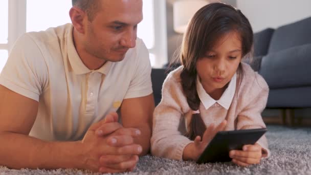 Baba ve kızı birlikte vakit geçiriyorlar ve evde oturma odasında yerde yatarken aile eğlencesi için tablet kullanıyorlar.. - Video, Çekim