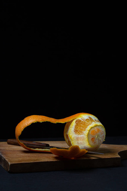 Oranje op een donkere achtergrond. Gepeld oranje en mes op een zwarte achtergrond. Sinaasappelschil mes - Foto, afbeelding