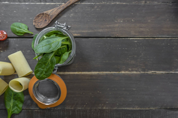 Top view spinach leaves in glass jar ,cherry tomatoes and tube penne pasta on vintage wooden background.Vegetarian organic ingredients.Italian food and healthy diet concept.Copy space place for text. - Φωτογραφία, εικόνα