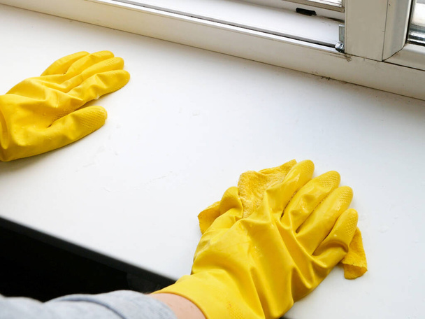 Γυναικείο χέρι σε κίτρινα γάντια που πλένουν το περβάζι. Υπηρεσίες καθαρισμού παραθύρων, κοντινό πλάνο  - Φωτογραφία, εικόνα