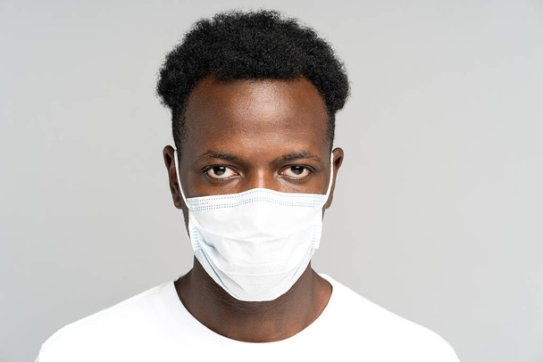 Jeune homme afro-américain portant un masque médical du visage, regardant la caméra, isolé sur fond gris - Photo, image