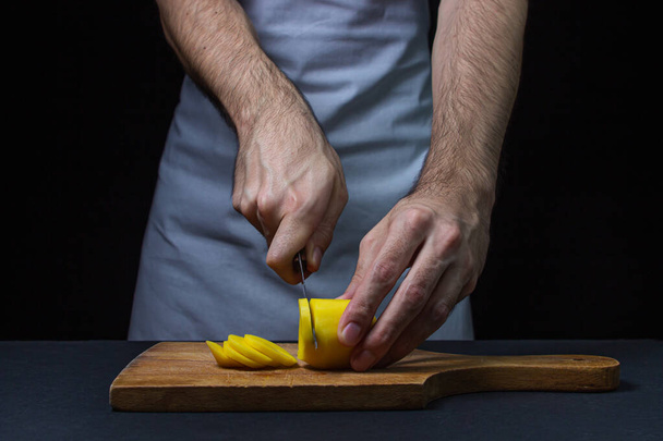 Batatas em um fundo escuro. O cozinheiro corta as batatas com uma faca. Mãos masculinas cortando batatas no fundo preto - Foto, Imagem