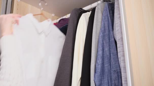 The concept of organizing space in the wardrobe. Clothes in dark and light shades are neatly hung in the closet. Woman's hand chooses clothes. - Footage, Video