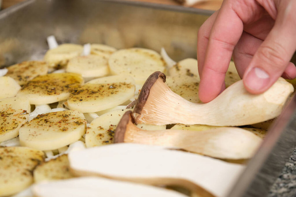 Close-up van de man handen plaatsen gesneden koning trompet champignons (pleurotus eryngii) over gekruide aardappelen en uien. Koken. Mediterrane voeding. - Foto, afbeelding