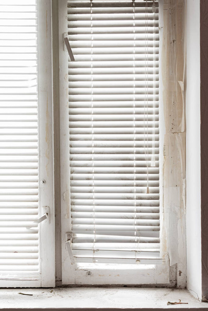 Holzfenster und weiße horizontale Jalousien. Fragment eines alten Holzfensters und eines schmutzigen alten Fenstersims. - Foto, Bild