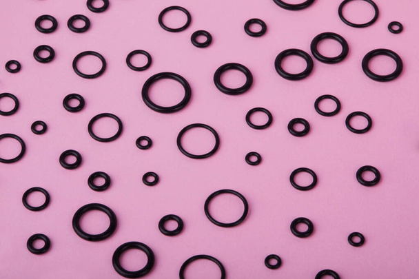 Black hydraulic and pneumatic o-ring seals of different sizes a pink  background. Rubber rings. Sealing gaskets for hydraulic joints. Rubber sealing rings for plumbing. Top view - Zdjęcie, obraz