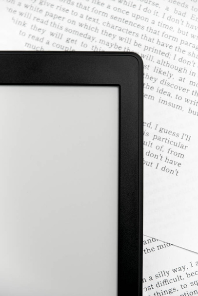 Detail van een elektronische lezer op vellen papier met tekst erop gedrukt. Begrippen: lezen en digitale technologie. Vlakke lay afbeelding met kopieerruimte. - Foto, afbeelding