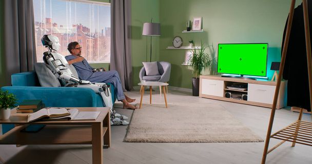 Зрелый мужчина смотрит телевизор с роботом - Фото, изображение