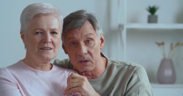 Starší živý emocionální pár sedí na gauči záznamy video zpráva šedovlasý muž ukazuje prstem směr na fotoaparát starší žena mávat rukama mluví chatování pomocí webové kamery během uzamčení - Záběry, video