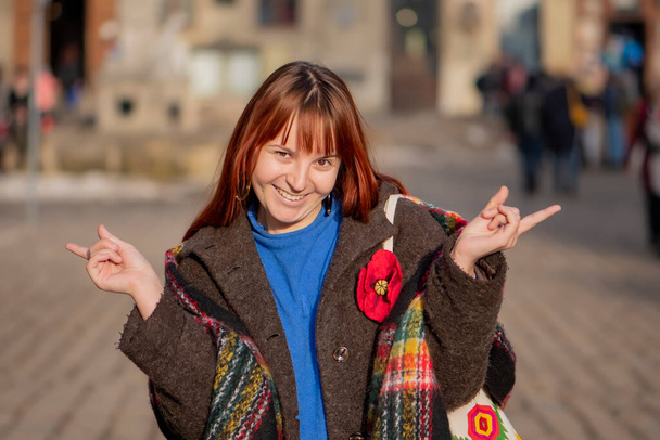 Γελώντας νεαρή γυναίκα 20-25 ετών με βαμμένα κόκκινα μαλλιά και λίγο υπέρβαρο στο φόντο της πόλης, γκρο πλαν πορτρέτο του δρόμου. Το χαρούμενο πρόσωπο ενός χοντρού κοριτσιού με φωτεινά ρούχα στο φως της ημέρας. - Φωτογραφία, εικόνα