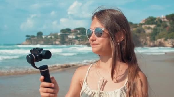 Nuori nainen nauhoittaa videon ulkona. Iloinen vlogger tyttö etsii kameraa rannalla - Materiaali, video