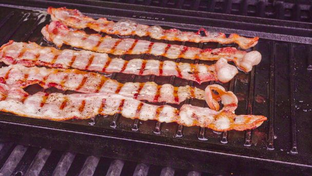 Cooking bacon stipes on an outdoor gas grill. - Photo, Image
