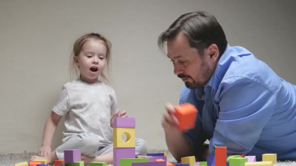Тато і дочка будують дім. Щаслива сім'я. Освітні ігри для дітей. Батько з дочкою грають в барвисті куби в дитячій кімнаті на підлозі. Навчання дітей іграми. - Кадри, відео