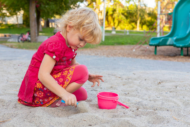 Kislány játszik a homokozóban lapáttal és vödörrel a parkban nyáron. - Fotó, kép