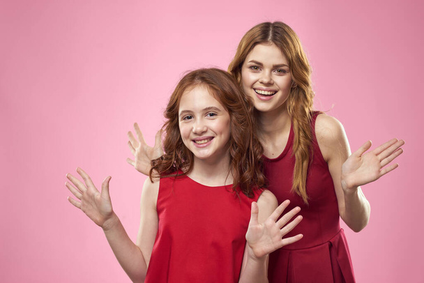 Cheerful mom and daughter wearing red dresses are standing next to joy family on pink background - Photo, Image