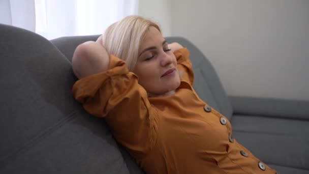Klidná mladá žena, která má zdravý denní spánek, odpočívá na gauči se zavřenýma rukama za hlavou, pokojná dívka spí, dýchá čerstvý vzduch, opírá se o pohodlnou pohovku doma - Záběry, video