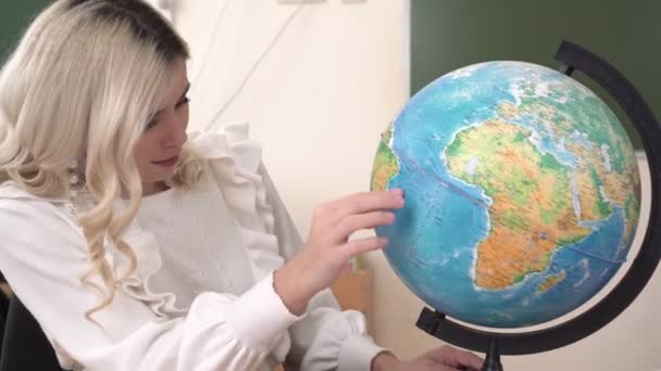 Молодая привлекательная женщина школьный учитель смотрит на глобус - Кадры, видео