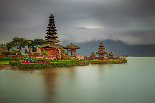 Храм Pura Ulun Danu Bratan на острове Бали. Красивый балийский храм на рассвете. Балийская достопримечательность. Облачное небо. Отражение воды. Медленный затвор. Озеро Фазан, Бали, Индонезия - Фото, изображение
