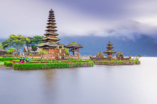 Świątynia Pura Ulun Danu Bratan na wyspie Bali. Piękna balijska świątynia podczas wschodu słońca. Balijski punkt orientacyjny. Chmurne niebo. Odbicie wody. Wolna prędkość migawki. Jezioro Bratan, Bali, Indonezja - Zdjęcie, obraz