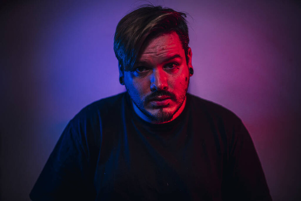 A portrait of an adult male with a beard and earlobe earrings under blue and red led lights - Photo, image
