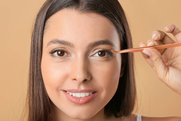 Beautiful young woman applying fake eyelashes against color background - Photo, Image