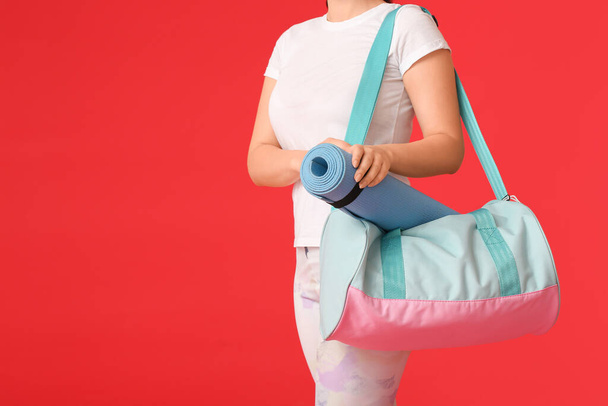 Mujer joven con bolsa de deporte y esterilla de yoga sobre fondo de color - Foto, Imagen