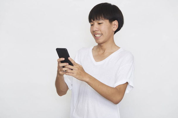 Fešák Mladý Asiat muž student textové zprávy pomocí smartphonu na lehkém pozadí. Kopírovat prostor a mockup - Fotografie, Obrázek