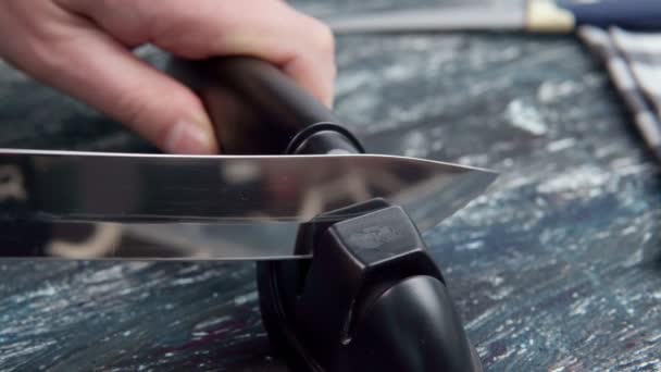 Een mes slijpen. Close-up van een man met behulp van een slijper om een mes te slijpen. - Video