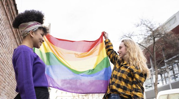 дві жінки з прапором гомосексуальної гордості, афро-жінка та інша блондинка, щасливі дві жінки з прапором гомосексуальної гордості, афро-жінка та інша блондинка, щаслива
 - Фото, зображення